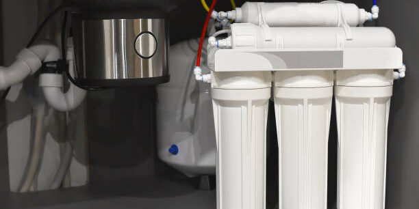 House water filtration system. Osmosis deionization system. Installation of water purification filters under kitchen sink in cupboard. Clear water concept. Small sharpness, possible granularity